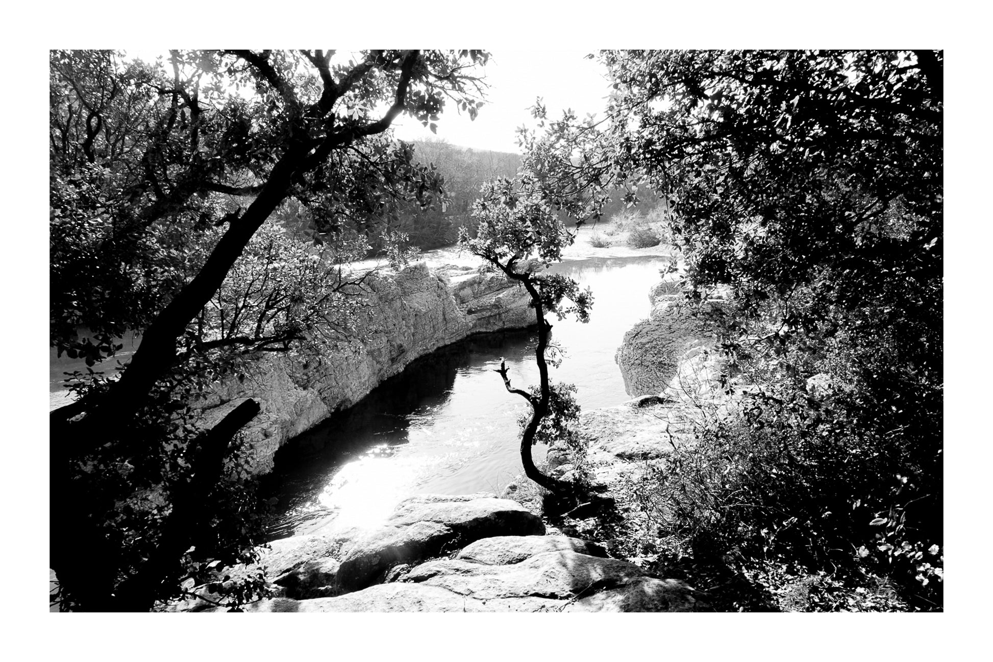 Courbe de la rivière Cèze vue à travers un encadrement d’arbres et de rochers à la cascade du Sautadet, noir et blanc avec bordure