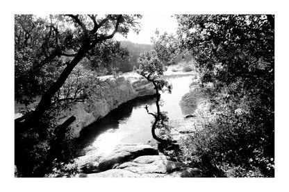Courbe de la rivière Cèze vue à travers un encadrement d’arbres et de rochers à la cascade du Sautadet, noir et blanc avec bordure