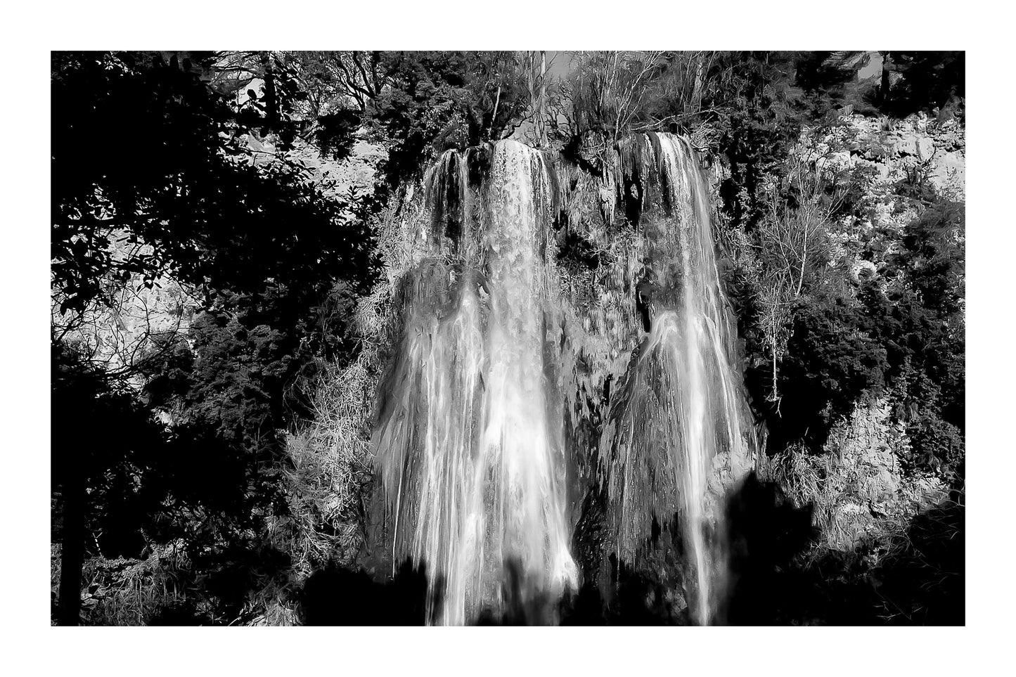 Grande cascade de Sillans tombant en rideaux blancs sur une paroi ocre et moussue, encadrée par la végétation, noir et blanc avec bordure
