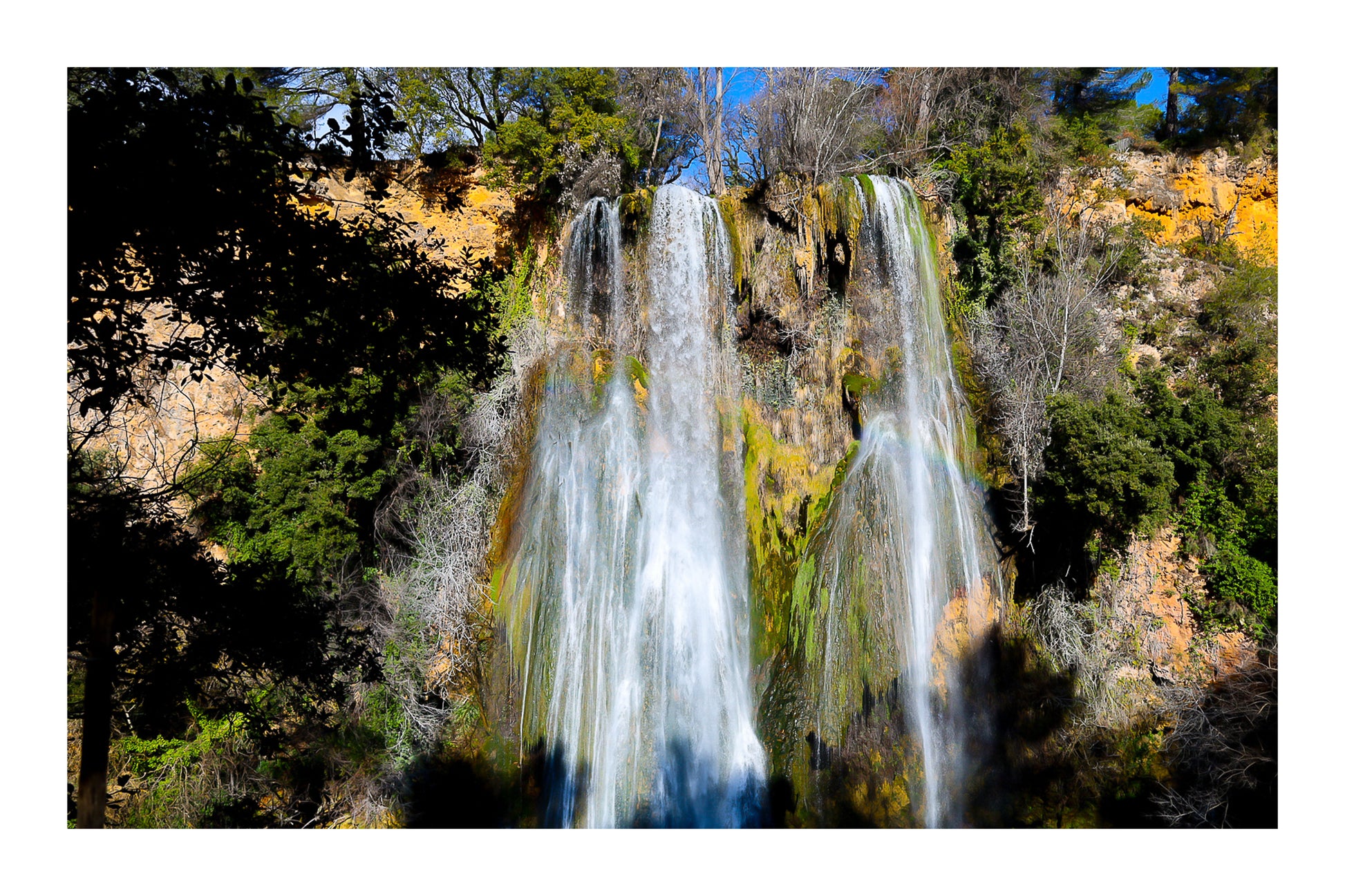 Grande cascade de Sillans tombant en rideaux blancs sur une paroi ocre et moussue, encadrée par la végétation avec bordure