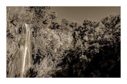 Paroi rocheuse orangée et pins verts dominant la cascade de Sillans sous un ciel bleu intense, version sépia avec bordure