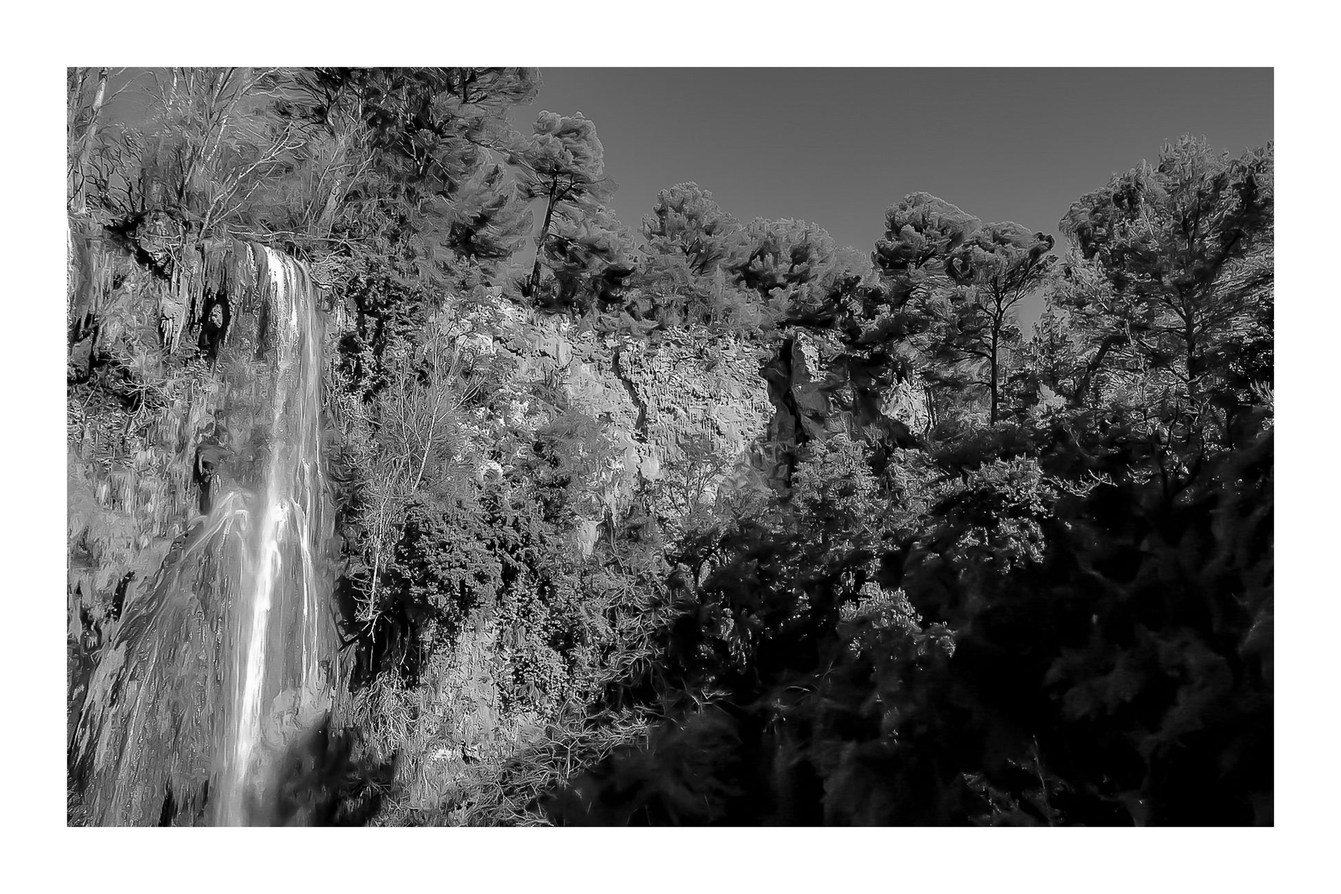 Paroi rocheuse orangée et pins verts dominant la cascade de Sillans sous un ciel bleu intense, version noir et blanc avec bordure