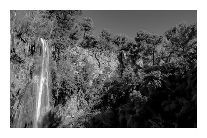 Paroi rocheuse orangée et pins verts dominant la cascade de Sillans sous un ciel bleu intense, version noir et blanc avec bordure