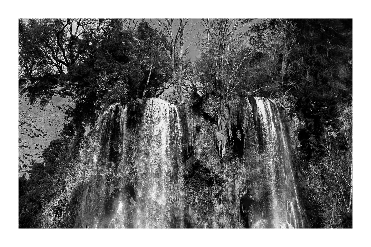 Deux pans de cascade à Sillans dévalant la falaise, entourés d’arbres nus et de mousse verte, version noir et blanc avec bordure
