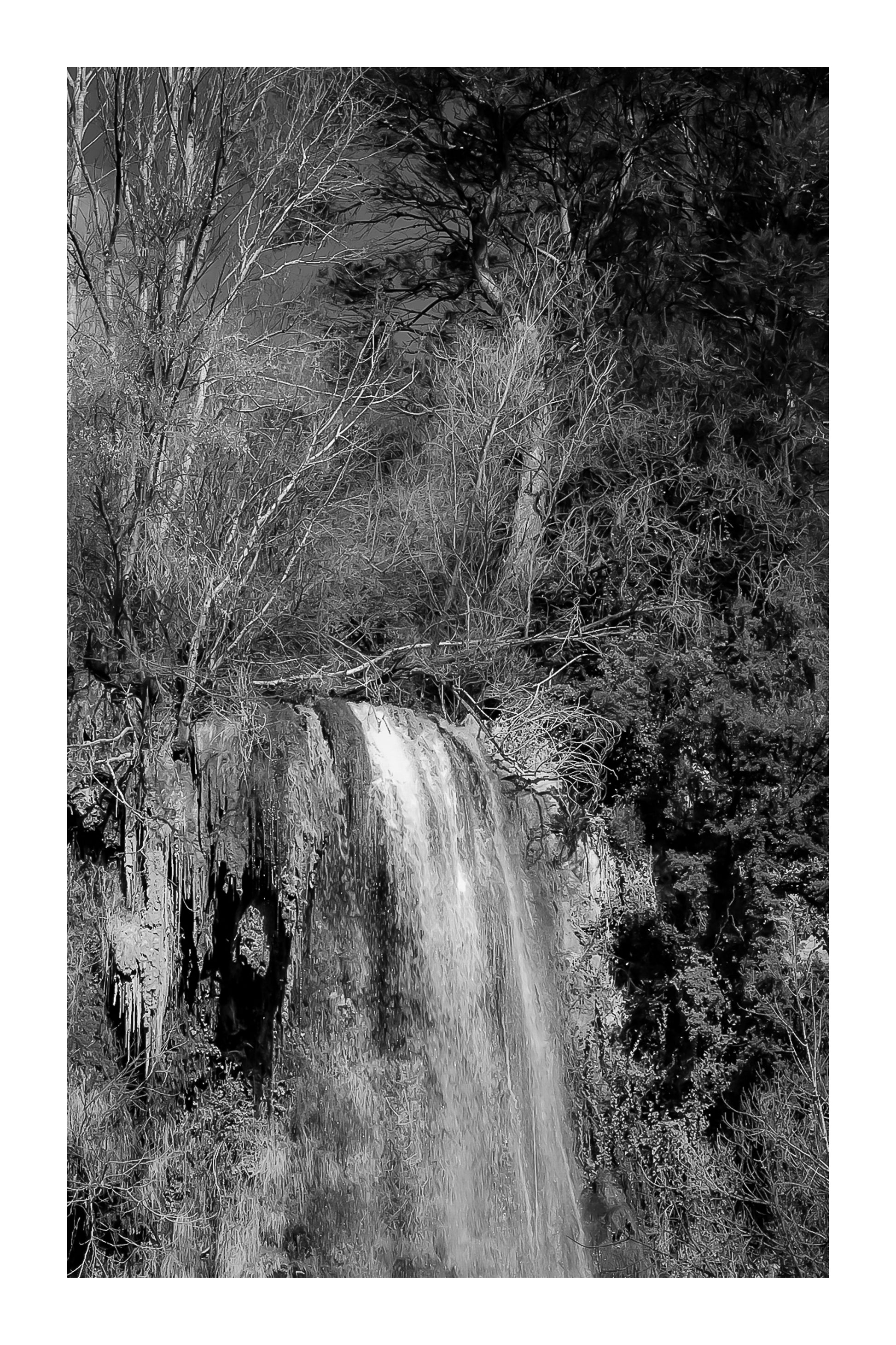 Gros plan vertical sur la cascade de Sillans avec eau ruisselante et mousses vertes accrochées à la falaise, noir et blanc avec bordure