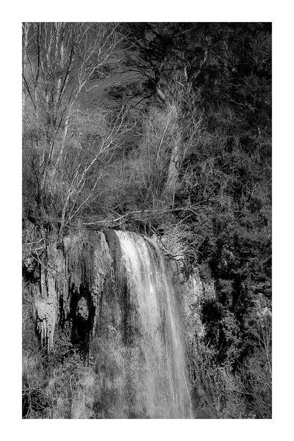 Gros plan vertical sur la cascade de Sillans avec eau ruisselante et mousses vertes accrochées à la falaise, noir et blanc avec bordure