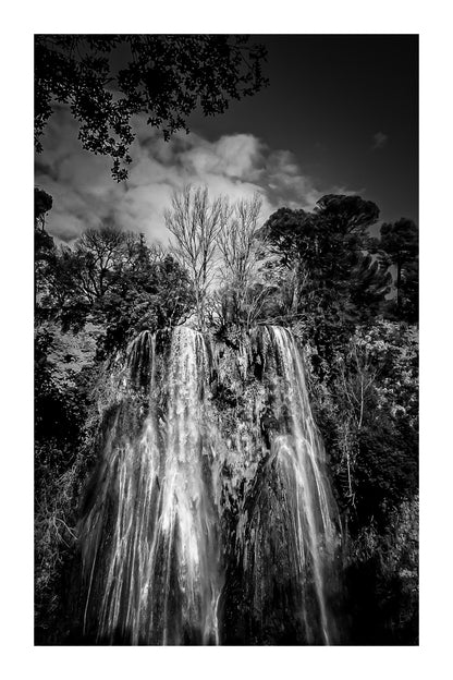 Haute cascade de Sillans se détachant sur un ciel bleu, encadrée par les arbres de la forêt, noir et blanc avec bordure