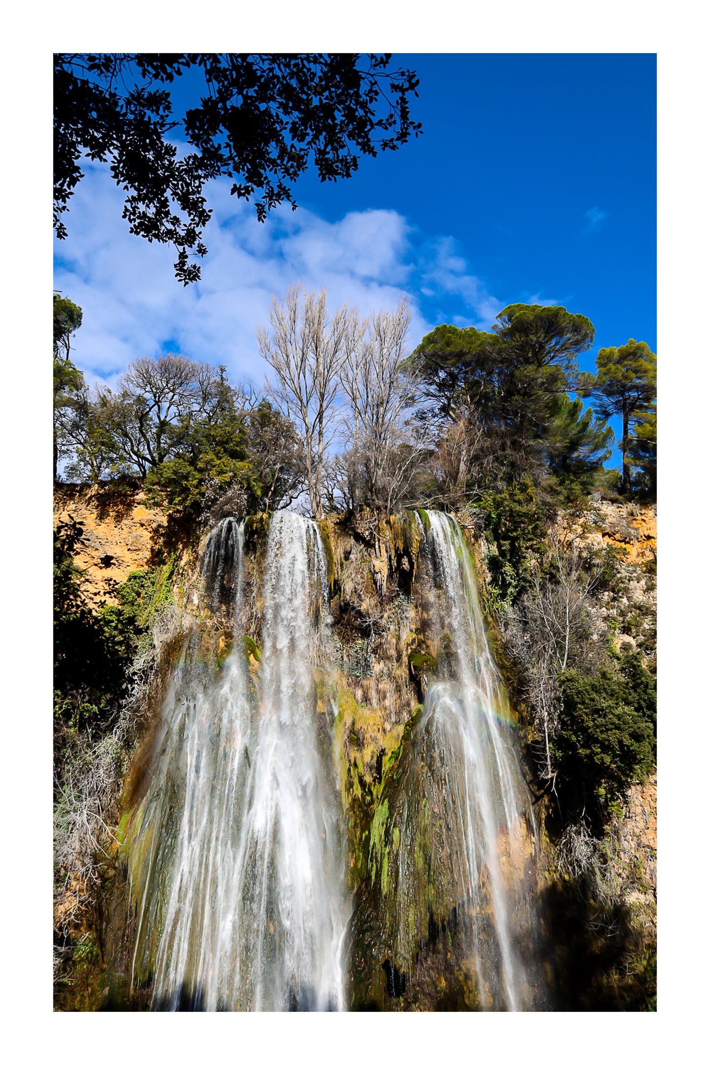 Haute cascade de Sillans se détachant sur un ciel bleu, encadrée par les arbres de la forêt avec bordure