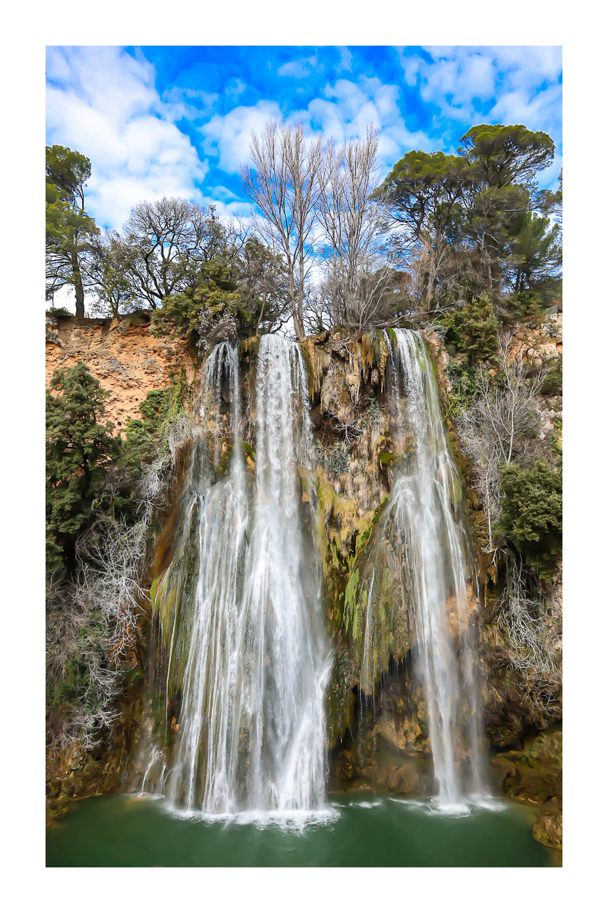 Grande cascade de Sillans se jetant dans un bassin vert émeraude entouré de falaises et de végétation avec bordure