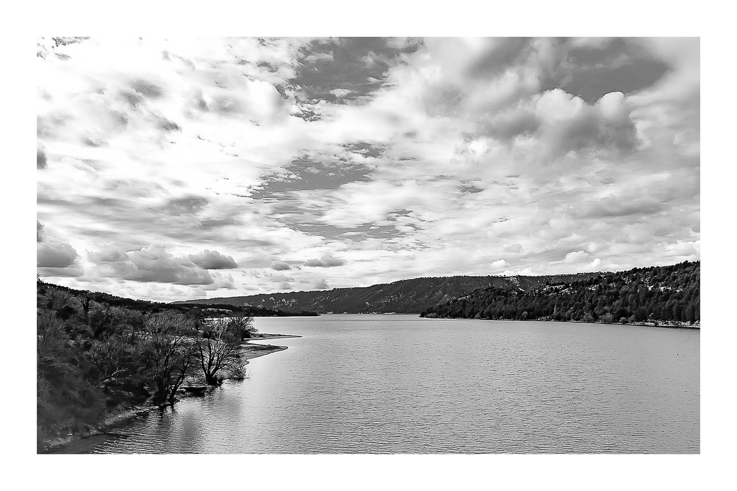 Large vue sur le lac de Sainte-Croix depuis un pont, rives boisées et grand ciel nuageux, noir et blanc et bordure
