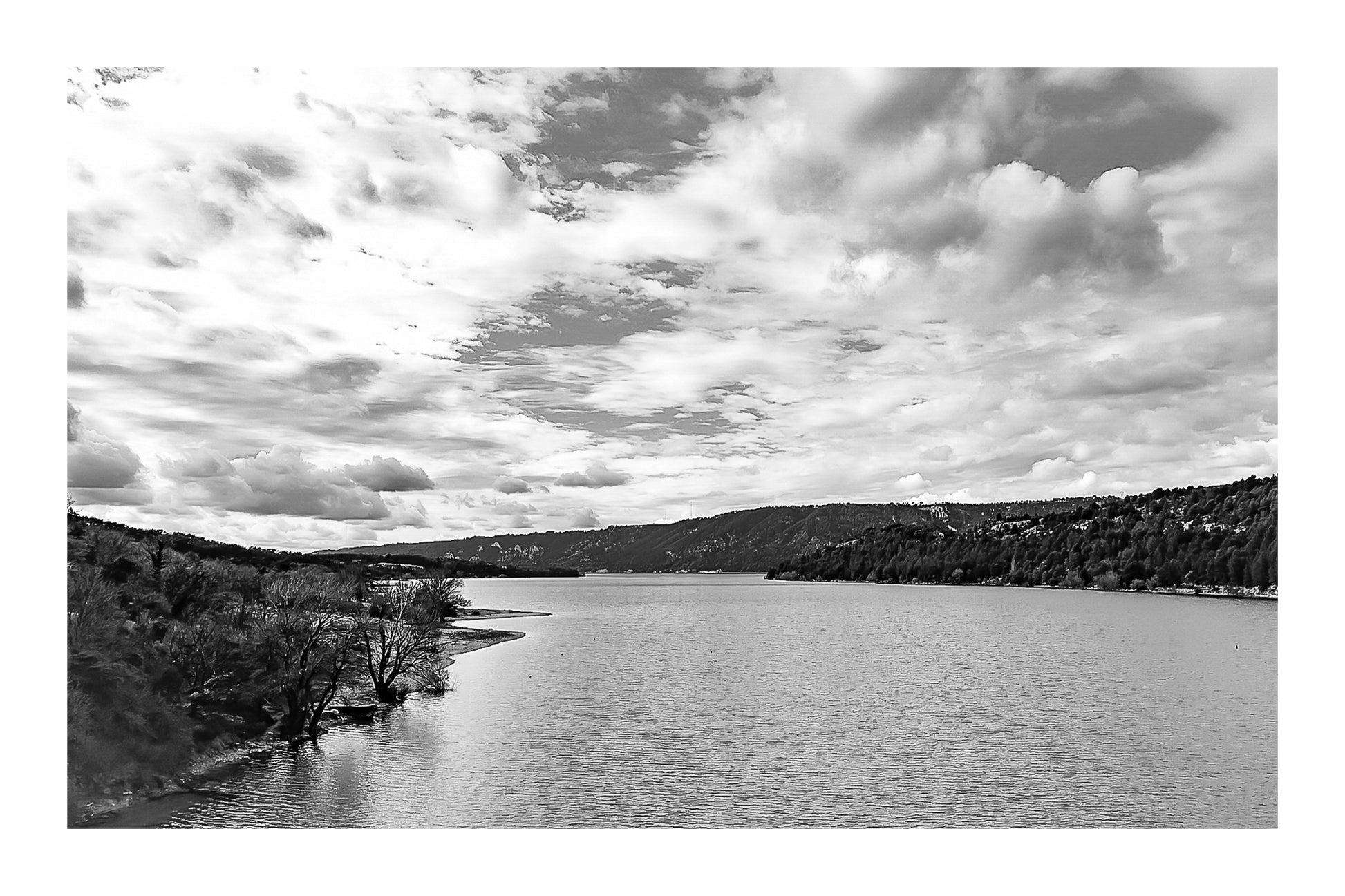 Large vue sur le lac de Sainte-Croix depuis un pont, rives boisées et grand ciel nuageux, noir et blanc et bordure