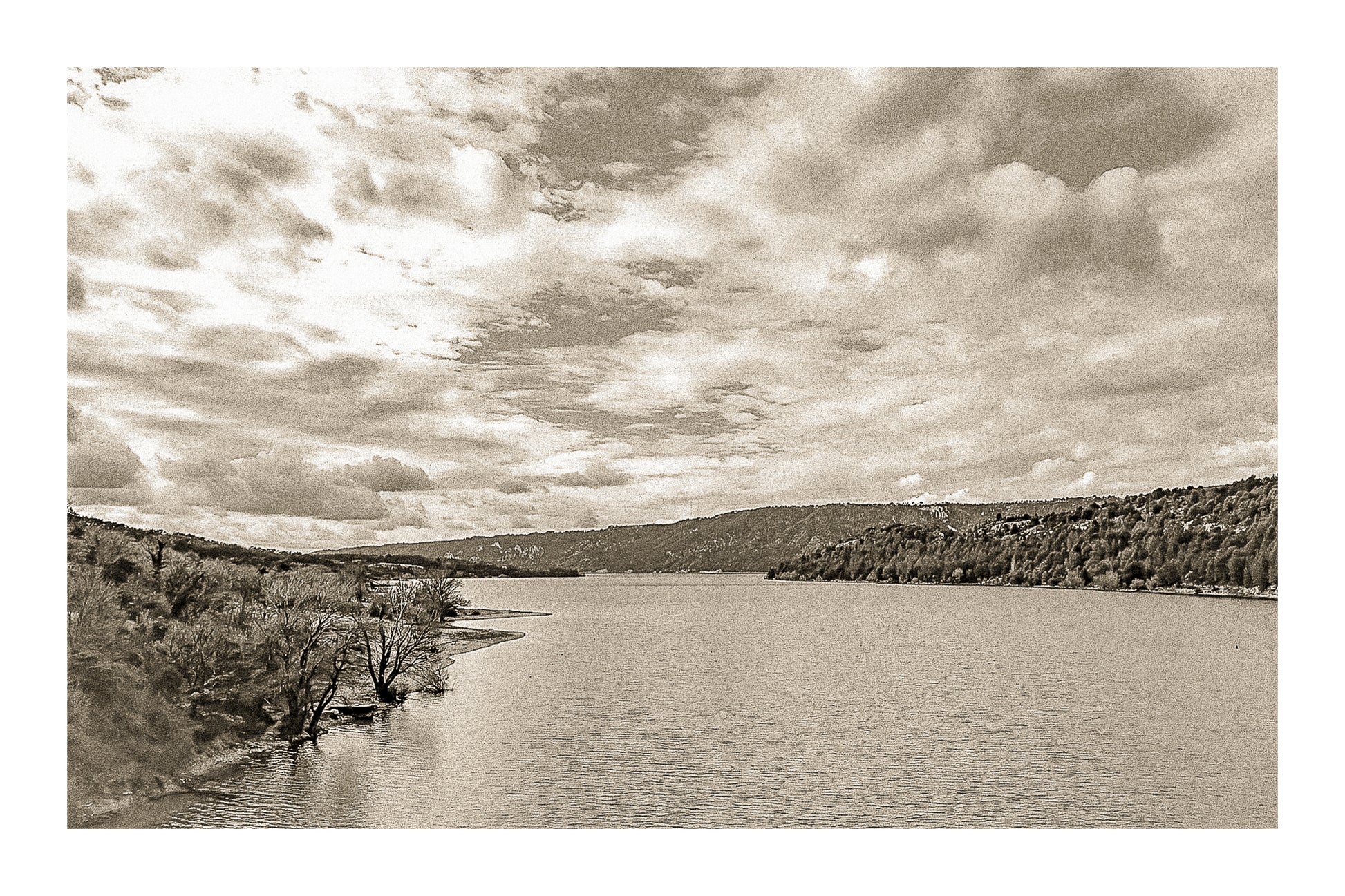 Large vue sur le lac de Sainte-Croix depuis un pont, rives boisées et grand ciel nuageux, vintage avec bordure