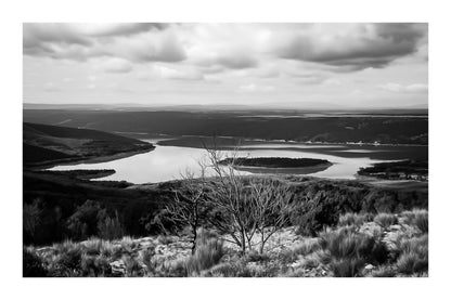Vue panoramique sur le lac de Sainte-Croix, bras d’eau sinueux et collines provençales sous un ciel nuageux, noir et blanc avec bordure