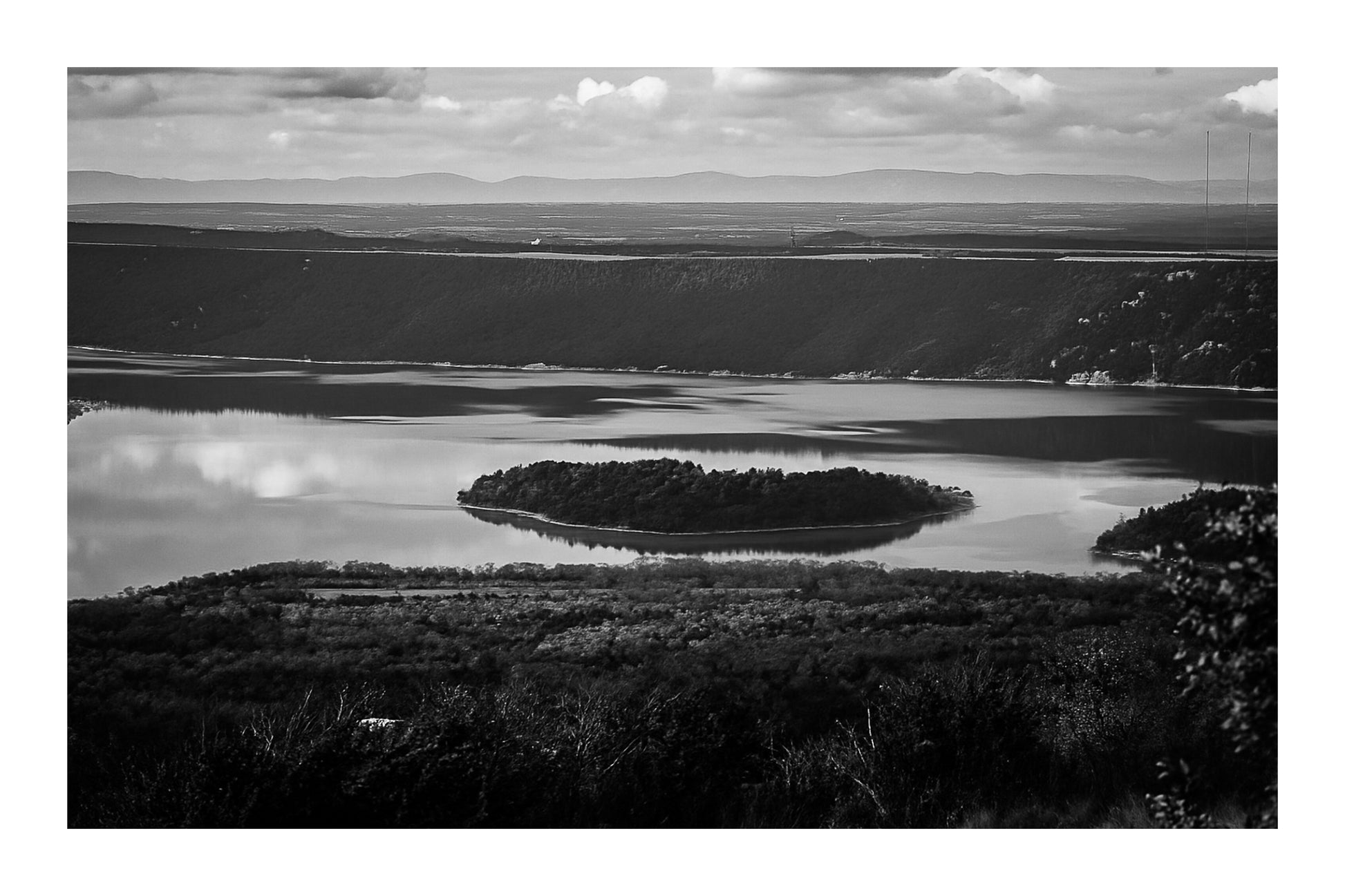 Îlot boisé flottant au centre du lac de Sainte-Croix, eaux calmes et reliefs sombres en arrière-plan, noir et lanc avec bordure