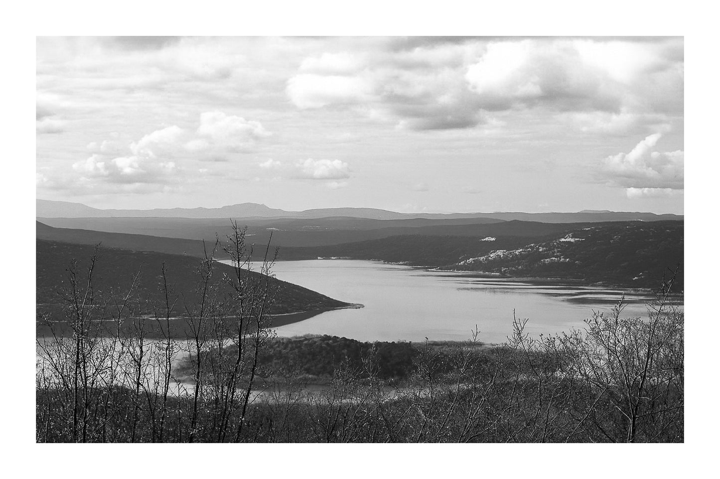 Long bras du lac de Sainte-Croix s’étirant entre collines et bosquets, sous un ciel nuageux, noir et blanc avec bordure