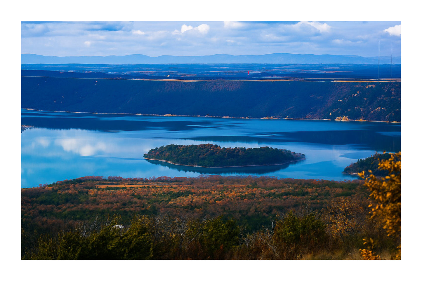 Îlot boisé flottant au centre du lac de Sainte-Croix, eaux calmes et reliefs sombres en arrière-plan avec bordure