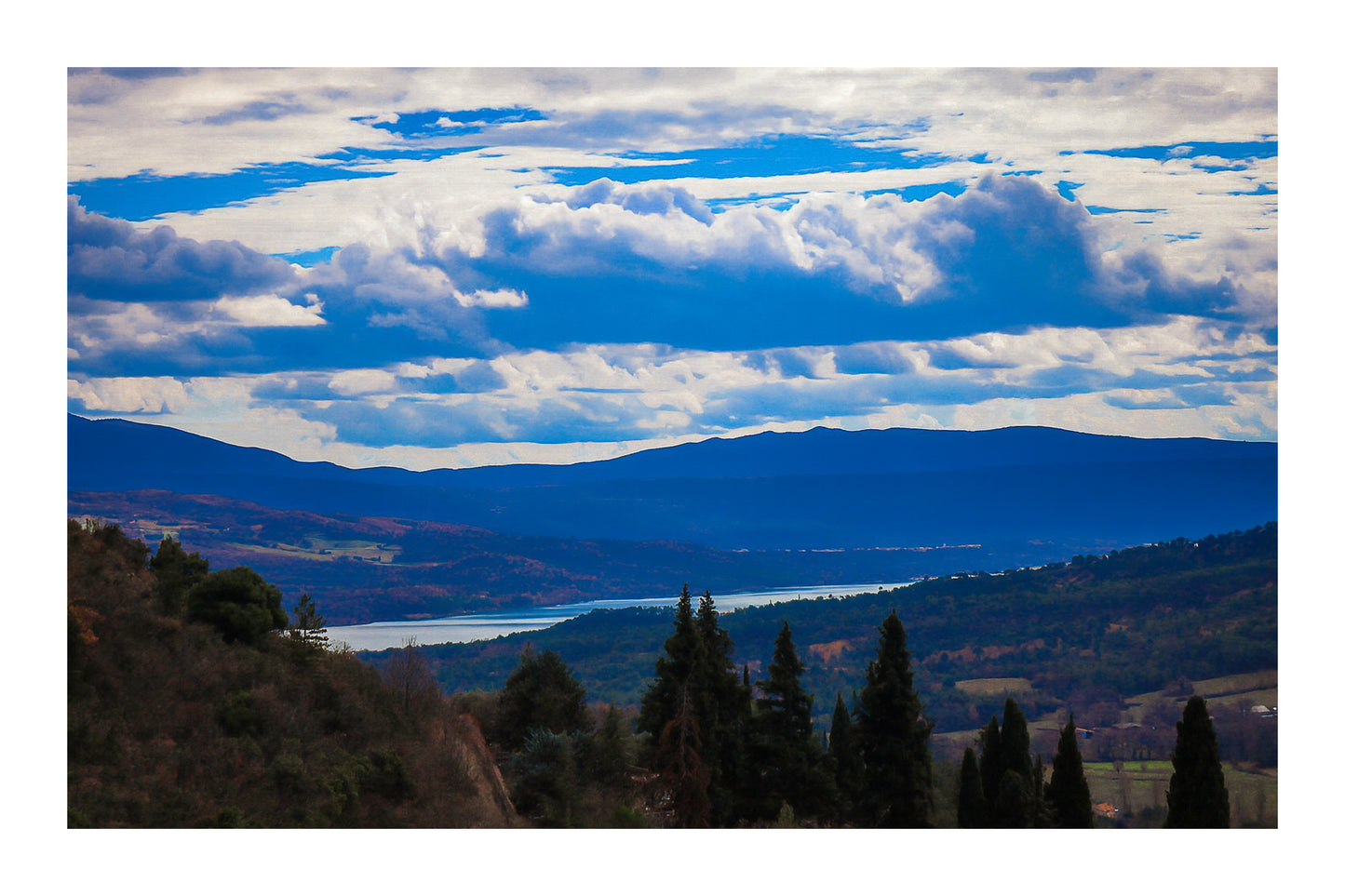 Vue lointaine sur le lac de Sainte-Croix entouré de collines, sous un ciel de nuages contrastés avec bordure