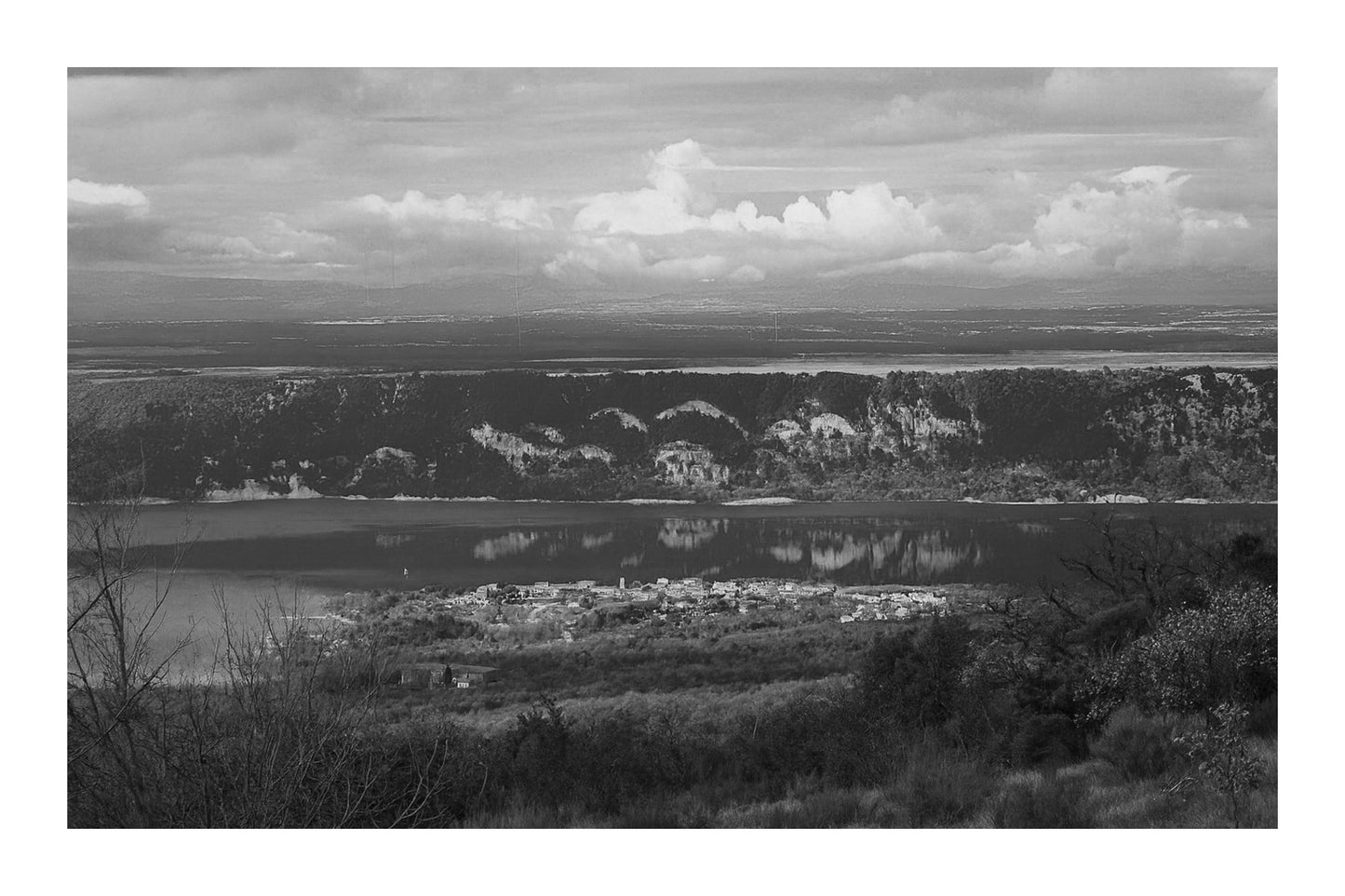 Village provençal posé au bord du lac de Sainte-Croix, falaises et reflets dorés sur l’eau calme, noir et blanc avec bordure