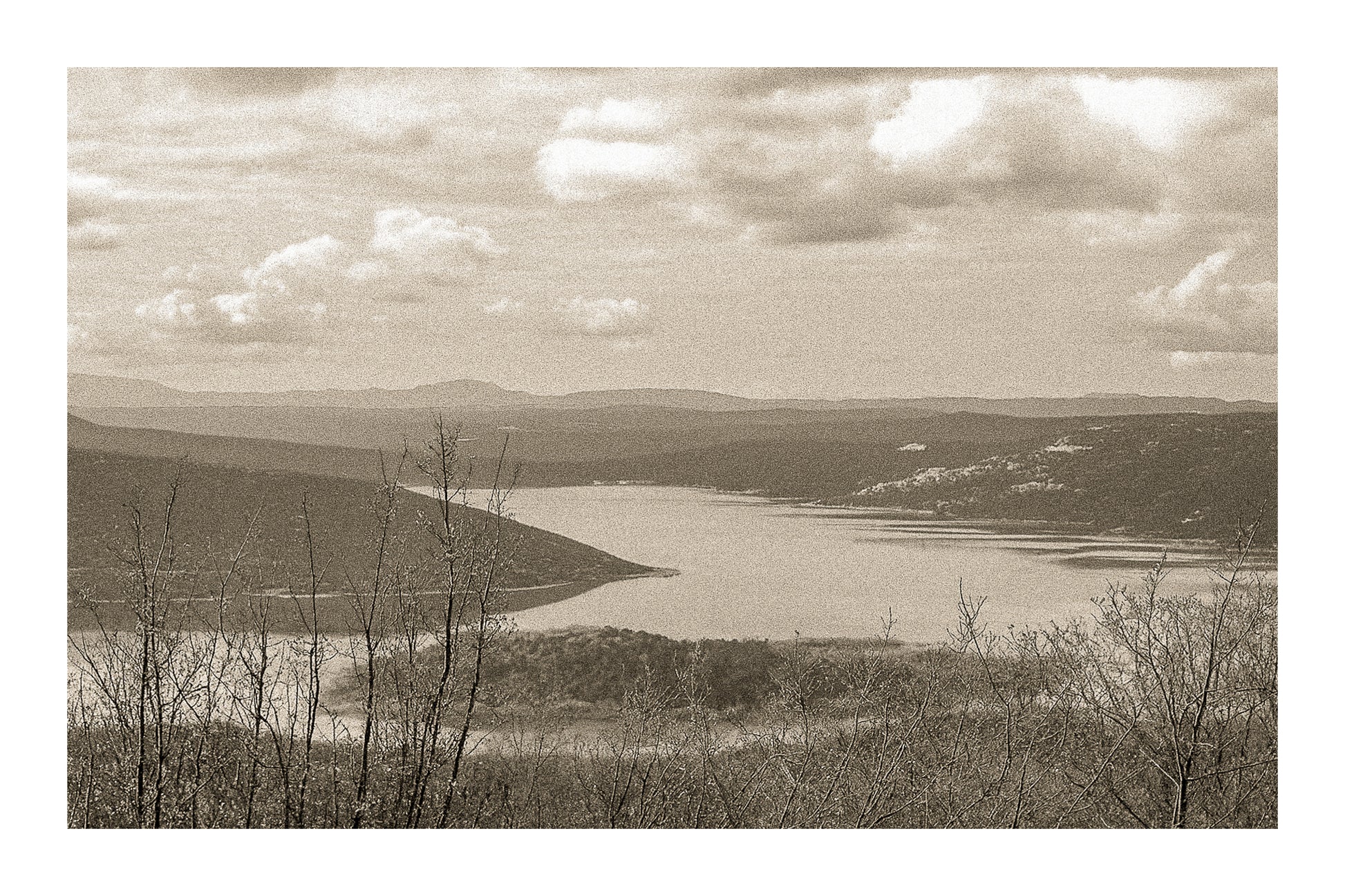 Long bras du lac de Sainte-Croix s’étirant entre collines et bosquets, sous un ciel nuageux, vintage avec bordure