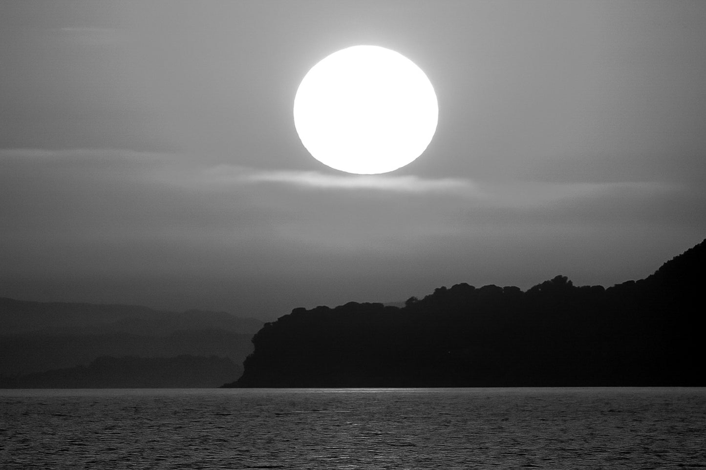 Gros soleil couchant orange au-dessus de la presqu’île de Giens vu depuis la plage de l’Almanarre, noir et blanc