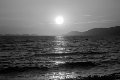 Coucher de soleil doré se reflétant sur la mer calme à la plage de l’Almanarre un soir d’été, noir et blanc