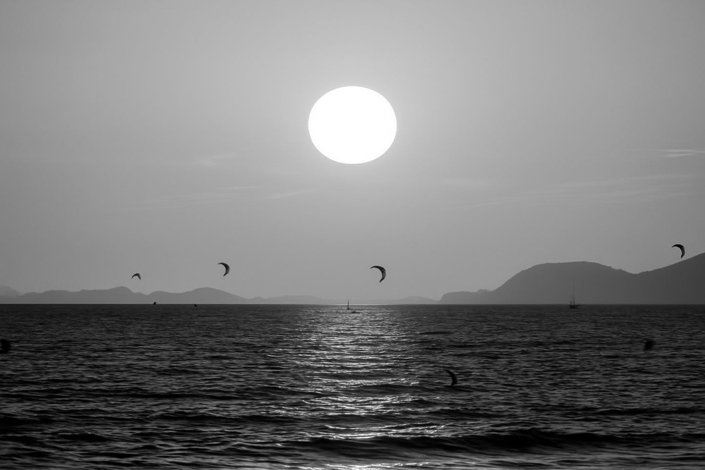 Soleil couchant orange au-dessus de la mer avec des ailes de kitesurf en silhouette à l’Almanarre, noir et blanc