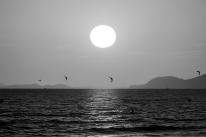 Soleil couchant orange au-dessus de la mer avec des ailes de kitesurf en silhouette à l’Almanarre, noir et blanc