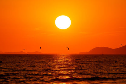 Soleil couchant orange au-dessus de la mer avec des ailes de kitesurf en silhouette à l’Almanarre