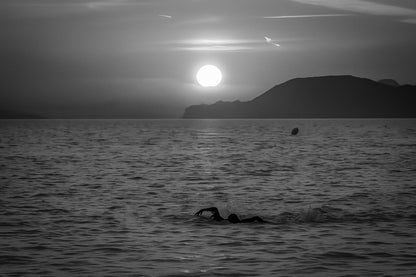 Silhouette de nageurs dans la mer rougeoyante au coucher du soleil à la plage de l’Almanarre, noir et blanc