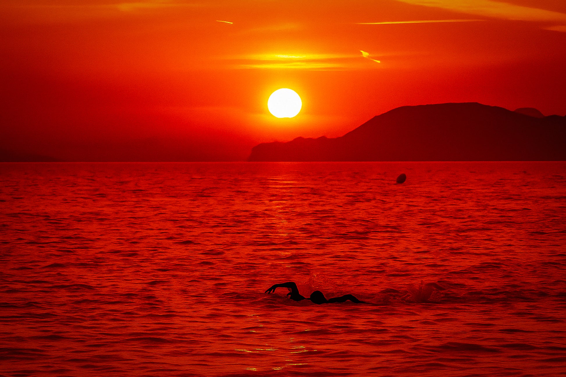 Silhouette de nageurs dans la mer rougeoyante au coucher du soleil à la plage de l’Almanarre