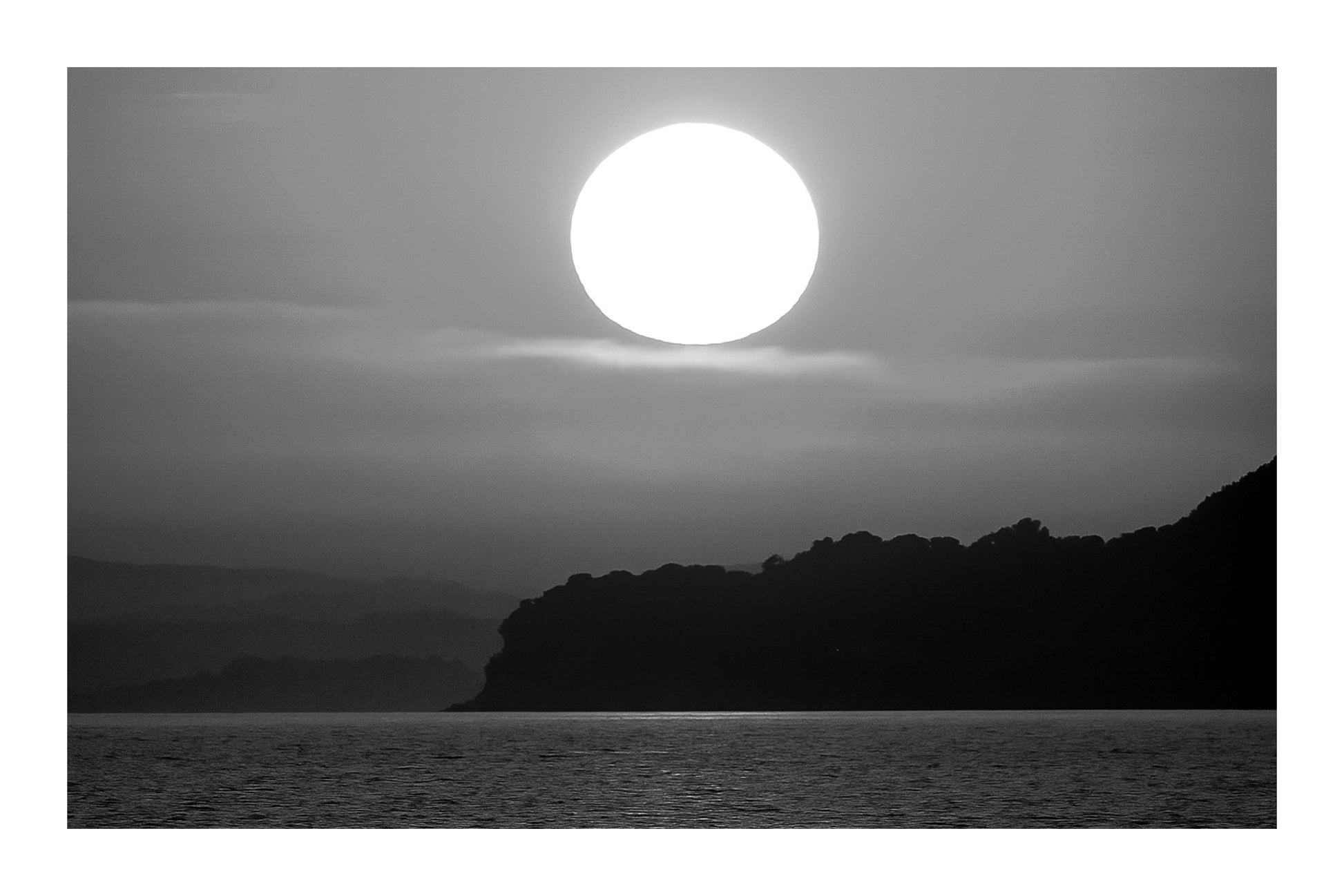 Gros soleil couchant orange au-dessus de la presqu’île de Giens vu depuis la plage de l’Almanarre, noir et blanc avec bordure