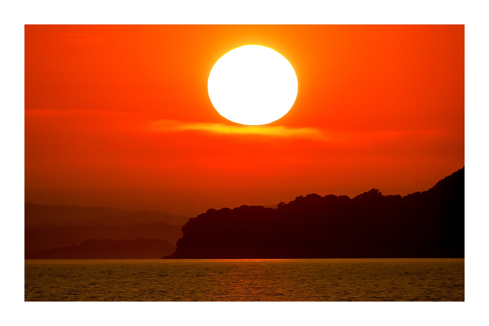 Gros soleil couchant orange au-dessus de la presqu’île de Giens vu depuis la plage de l’Almanarre, avec bordure