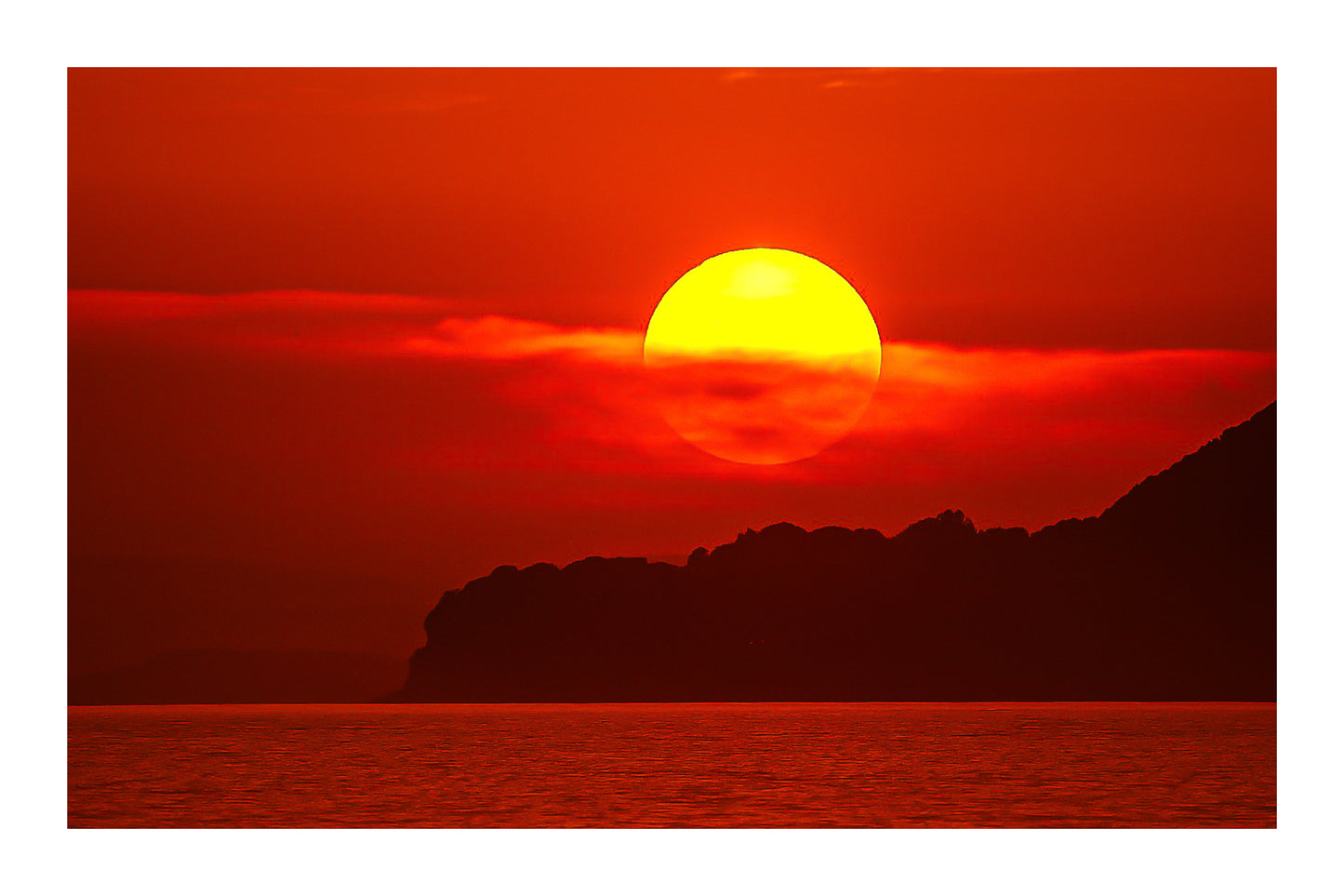 Gros plan sur le soleil rougeoyant partiellement voilé par un nuage au-dessus de la silhouette sombre de Giens avec bordure