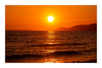 Coucher de soleil doré se reflétant sur la mer calme à la plage de l’Almanarre un soir d’été avec bordure