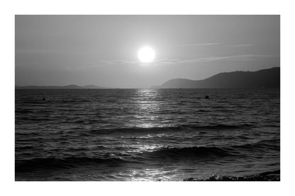Coucher de soleil doré se reflétant sur la mer calme à la plage de l’Almanarre un soir d’été, noir et blanc avec bordure
