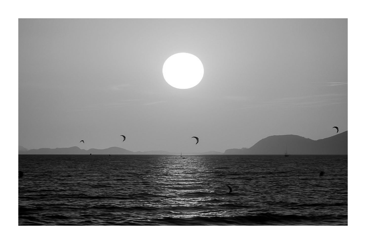 Soleil couchant orange au-dessus de la mer avec des ailes de kitesurf en silhouette à l’Almanarre, noir et blanc avec bordure