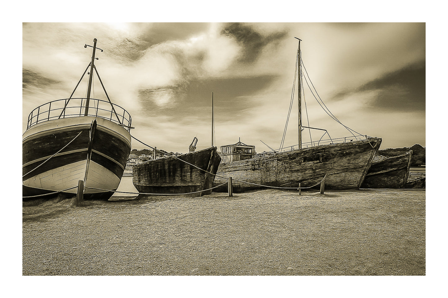 Trois bateaux en bois alignés sur la grève à Camaret, ciel nuageux et port en arrière-plan, vintage avec bordure