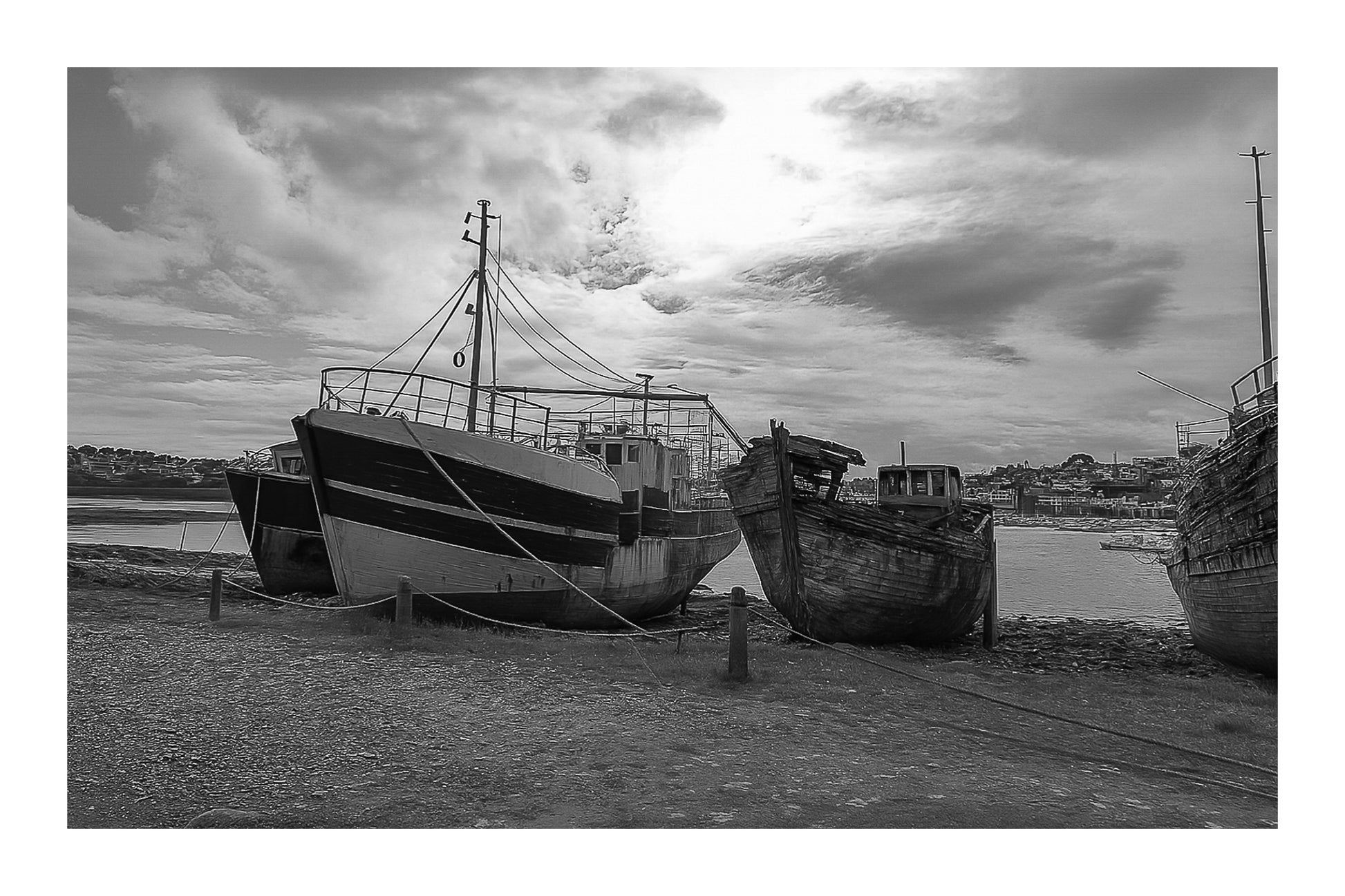 Bateau plus récent sur la gauche et coque déchiquetée à droite sur la grève de Camaret, ciel lumineux, noir et blanc avec bordure