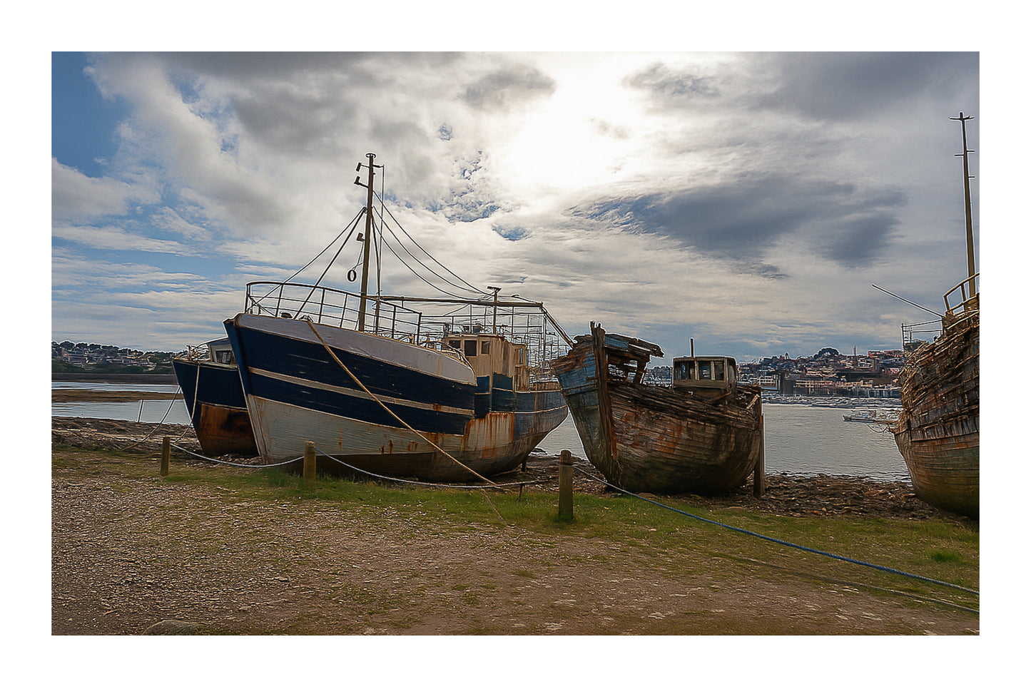 Bateau plus récent sur la gauche et coque déchiquetée à droite sur la grève de Camaret, ciel lumineux, avec bordure