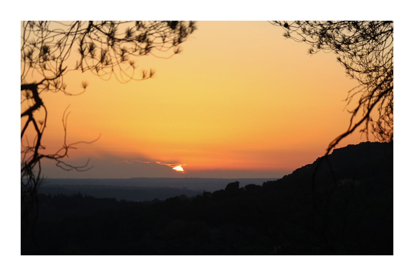 Disque solaire disparaissant derrière un lointain nuage, encadré par des branches à Bibemus avec bordure