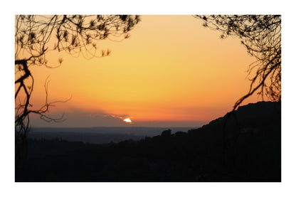 Disque solaire disparaissant derrière un lointain nuage, encadré par des branches à Bibemus avec bordure