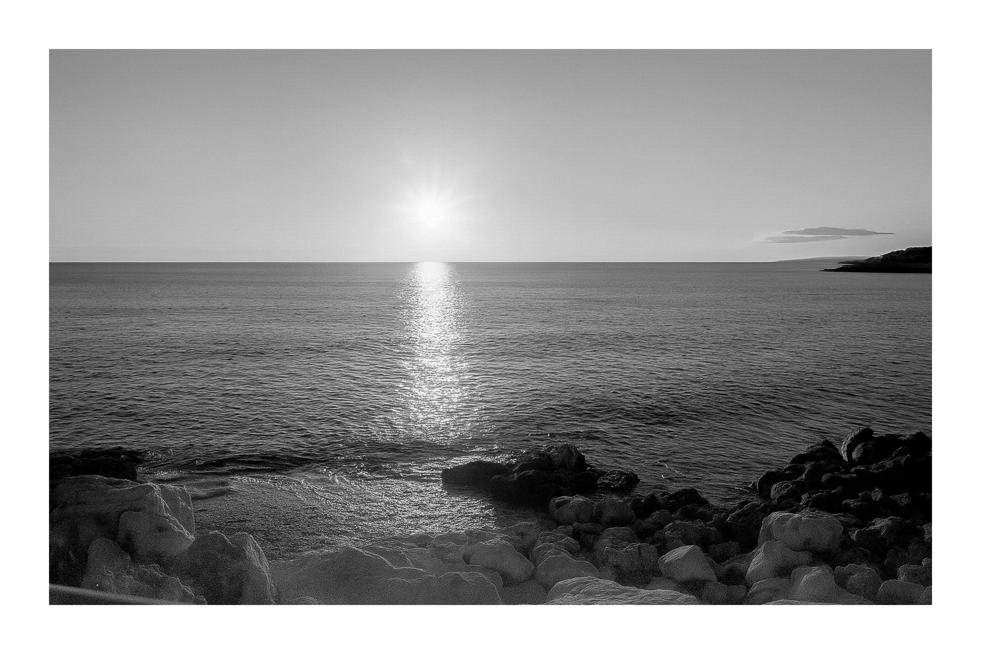 coucher de soleil à Carry-le-Rouet avec reflet doré sur la mer et premiers plans rocheux, noir et blanc avec bordure