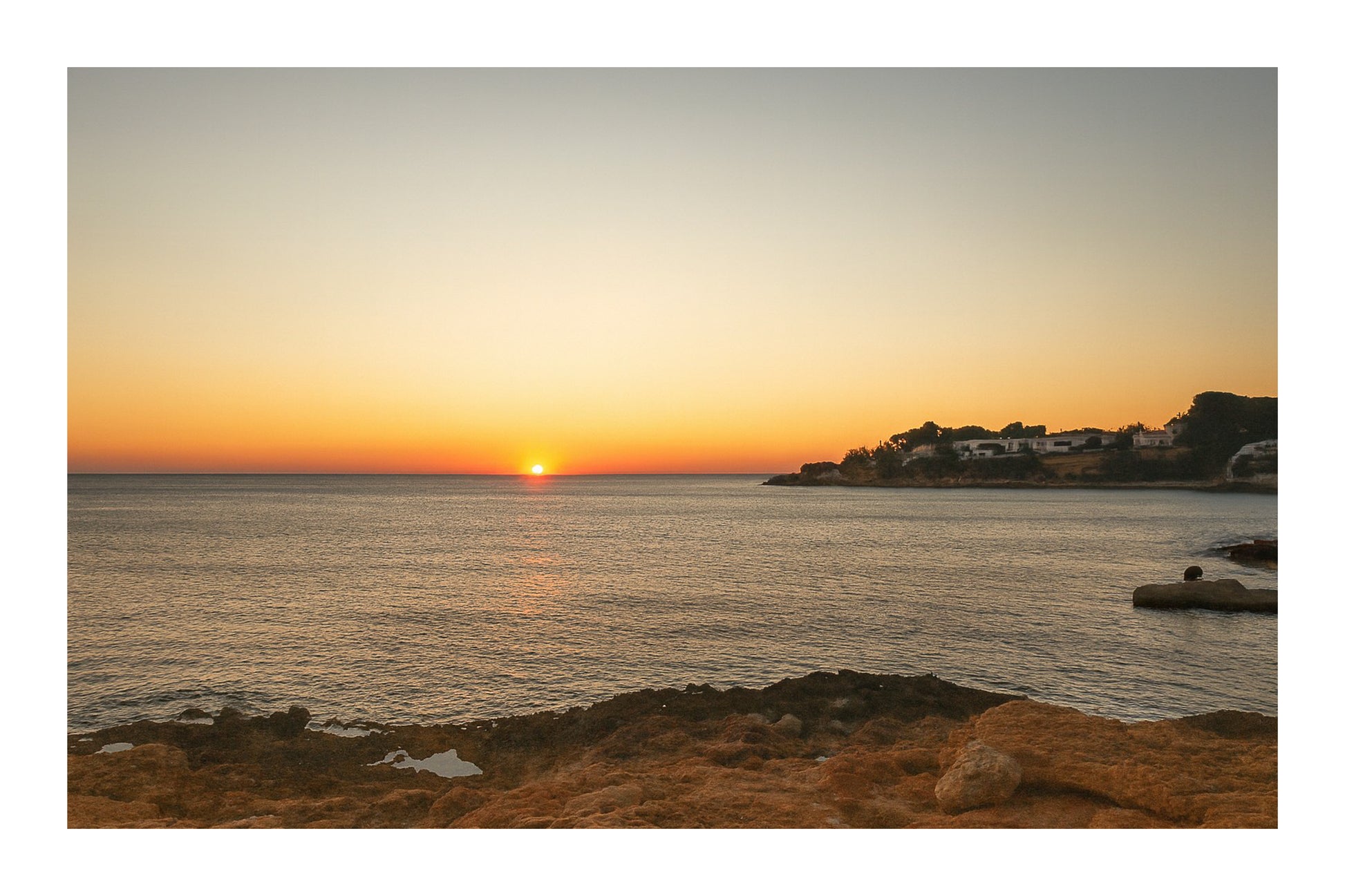 soleil à l’horizon éclairant une anse rocheuse et le village de Carry-le-Rouet avec bordure