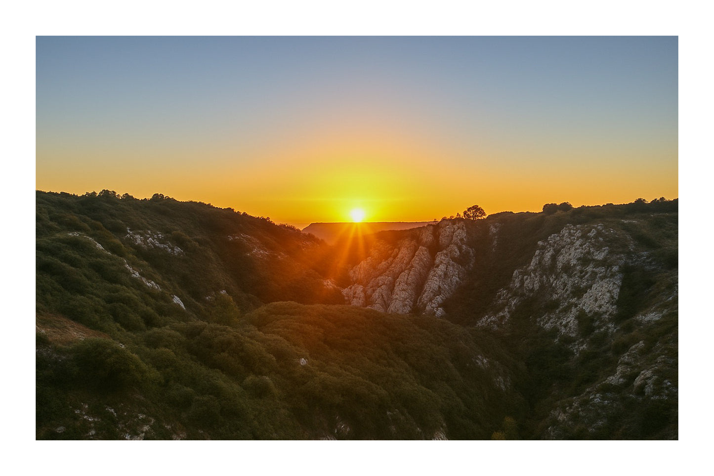Étoile solaire à l’horizon avec faisceaux lumineux au centre d’un cirque rocheux, vue panoramique depuis Bimont avec bordure