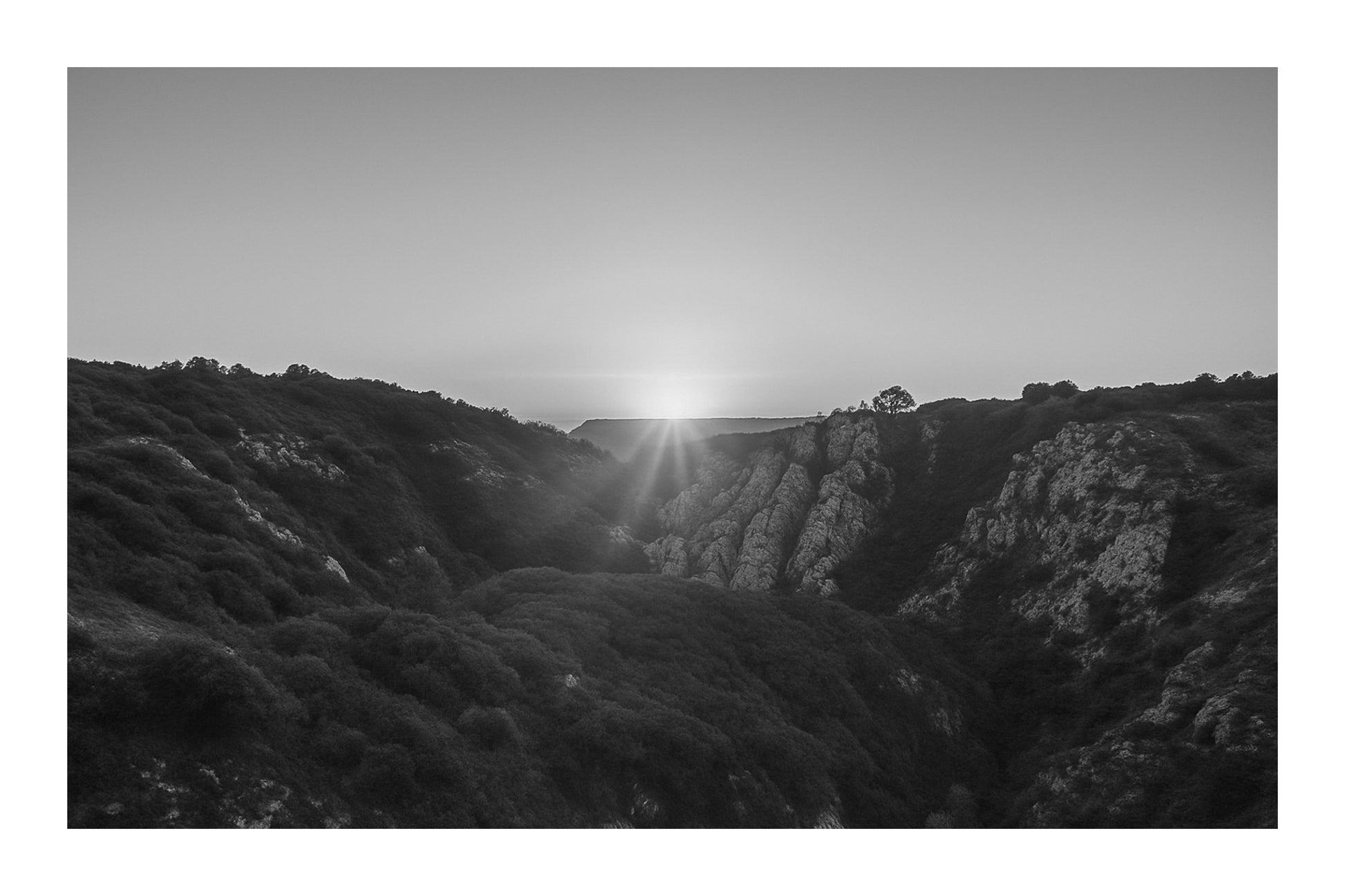 Étoile solaire à l’horizon avec faisceaux lumineux au centre d’un cirque rocheux, vue panoramique depuis Bimont, noir et blanc avec bordure