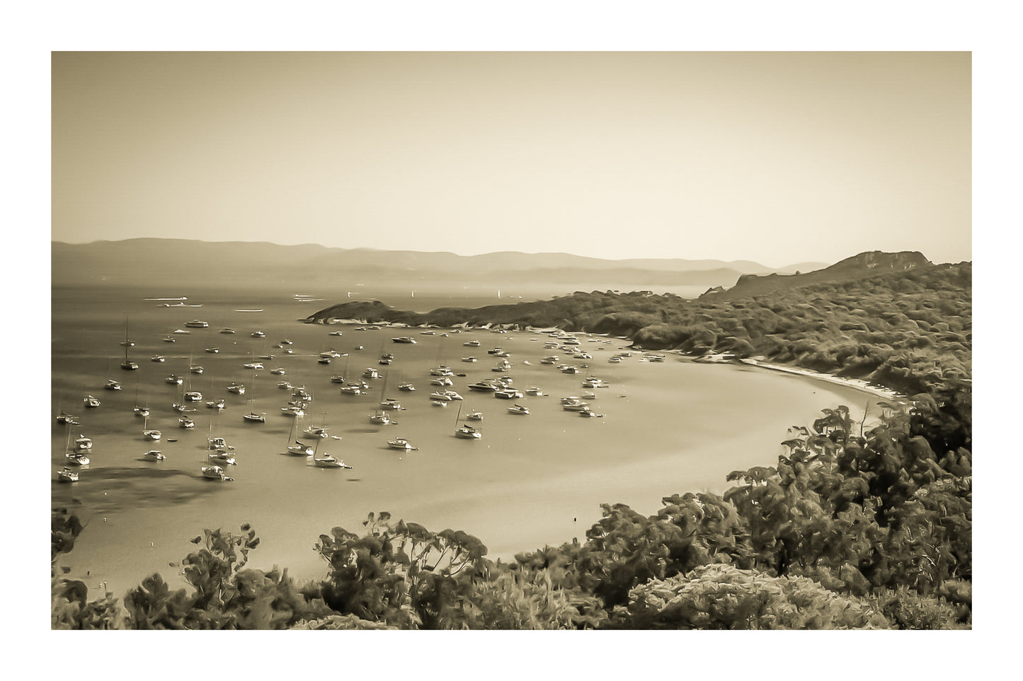 Vue plongeante sur la grande baie de Porquerolles avec de nombreux bateaux ancrés dans une eau turquoise sous un ciel d’été, vintage avec bordure
