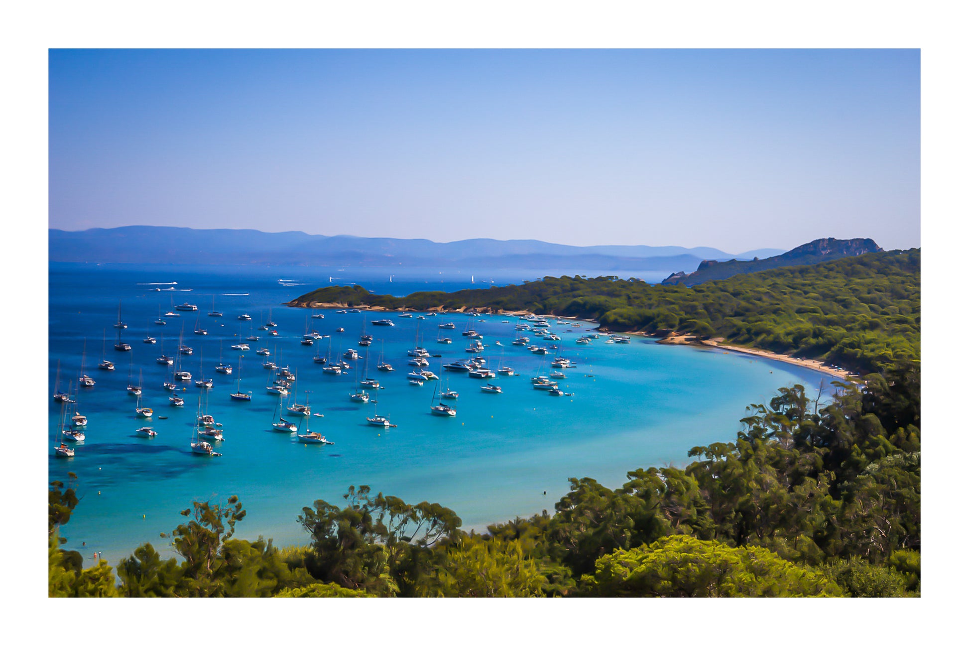 Vue plongeante sur la grande baie de Porquerolles avec de nombreux bateaux ancrés dans une eau turquoise sous un ciel d’été avec bordure