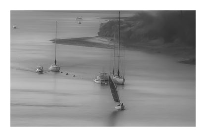 Voile rouge naviguant le long d’une file de bateaux au mouillage, noir et blanc avec bordure