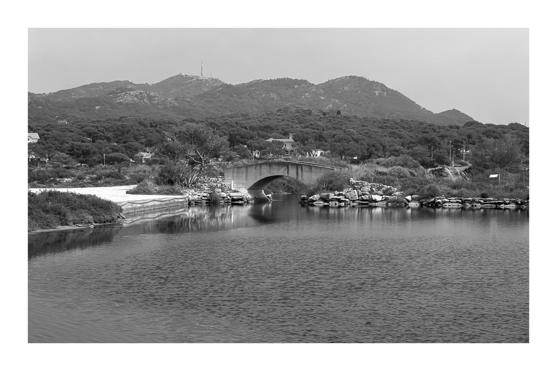 Petit pont en arc sur le canal intérieur des Embiez avec collines en arrière-plan, noir et blanc avec bordure