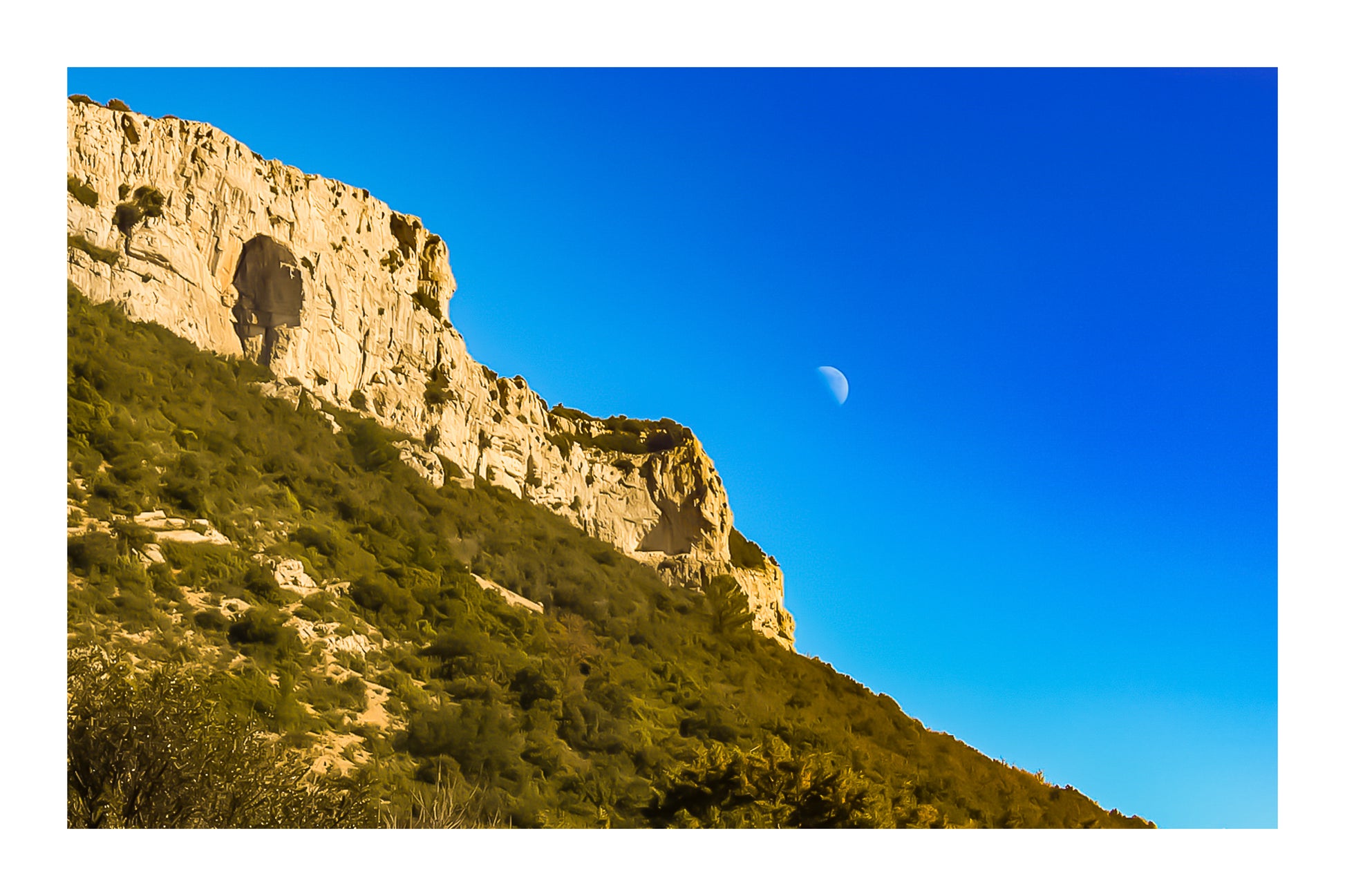 Falaise calcaire de la Sainte-Baume baignée de lumière chaude avec la lune accrochée dans un ciel bleu profond avec bordure